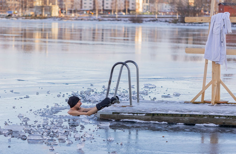 A man stepping out of icy water beside a wooden dock with a towel