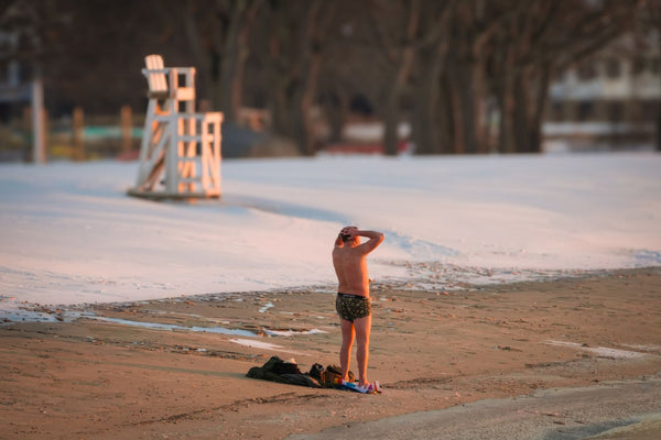 A person on a snowy beach at sunrise before a cold plunge