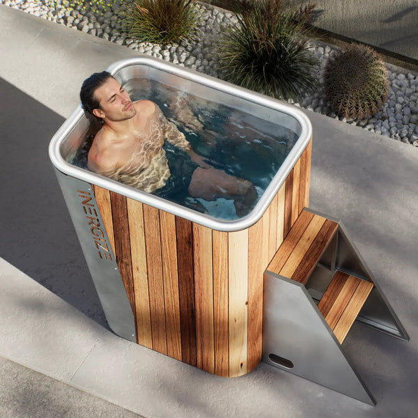 Man seated shoulder-deep in the Inergize Spire cold plunge, a cedar and stainless steel tub on a patio